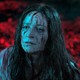 A woman with blood splattered on her face in front of a red background looks distraught in a scene from the movie Censor.